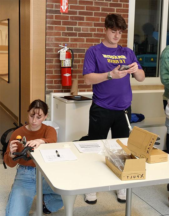 two students, one sitting at a desk operating a small catapult